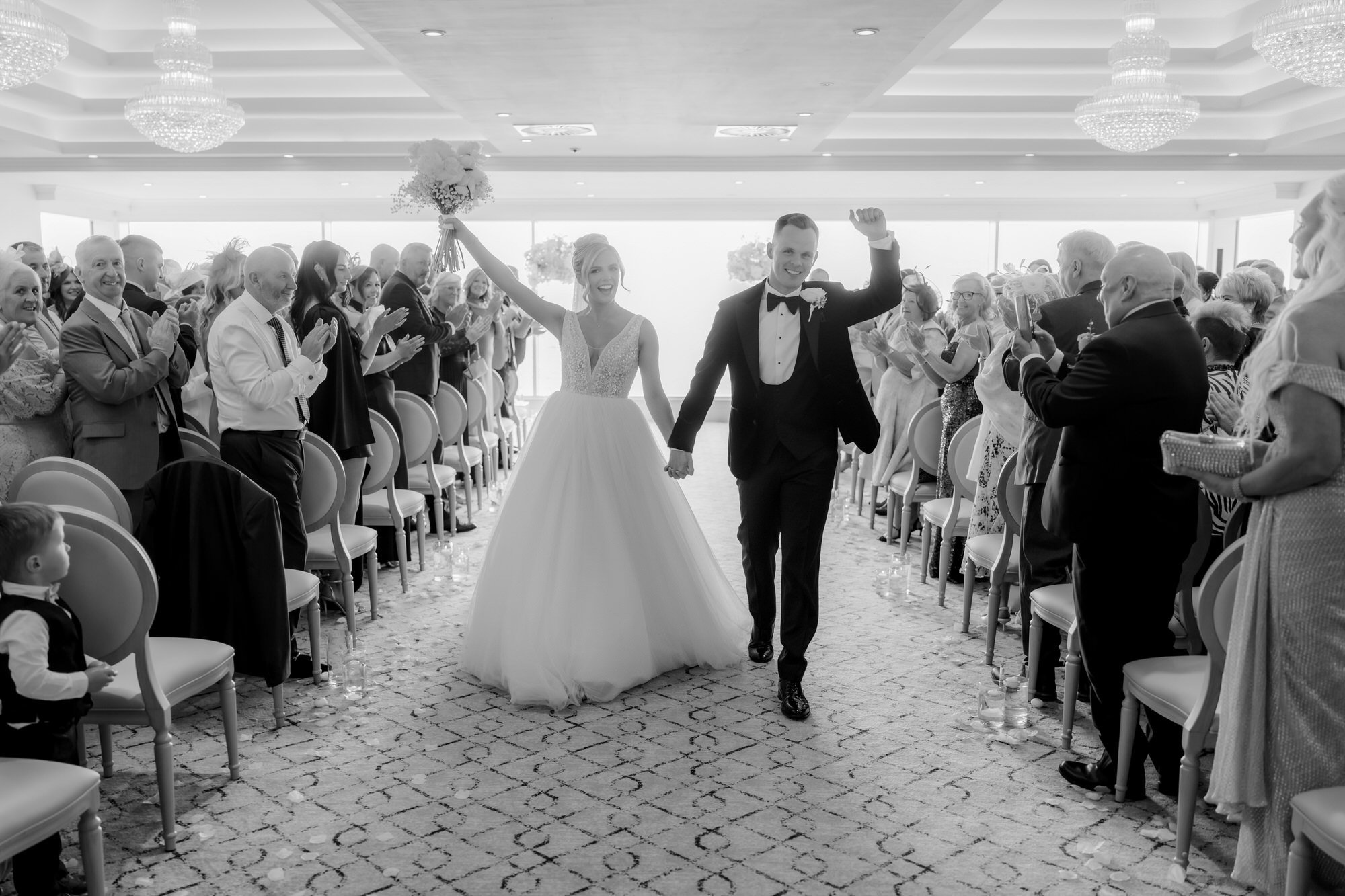The newlyweds walking back down the aisle to cheers in black and white.