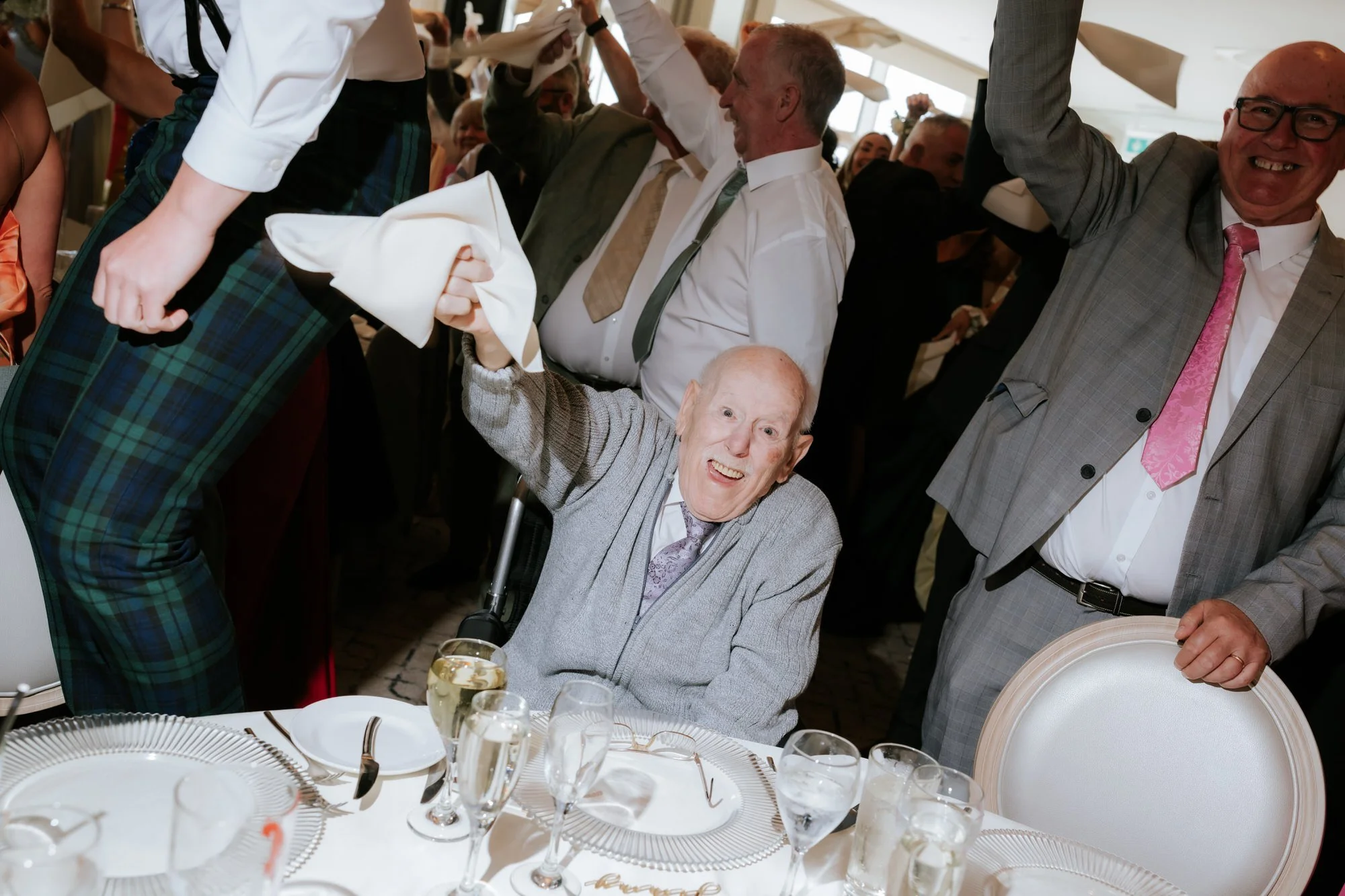 A guest in a wheelchair joining the celebrations with a raised napkin.
