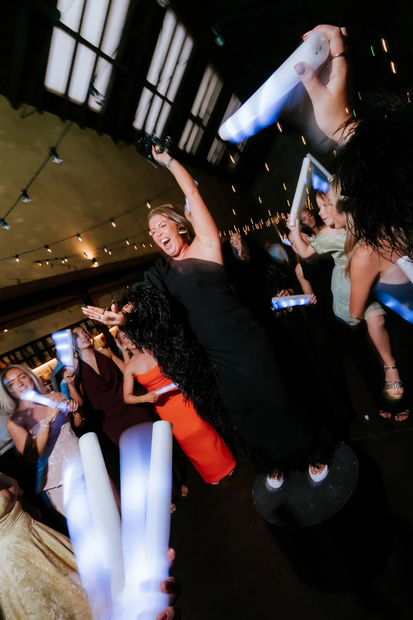 A guest dancing with her arm raised as glow sticks light up the party.