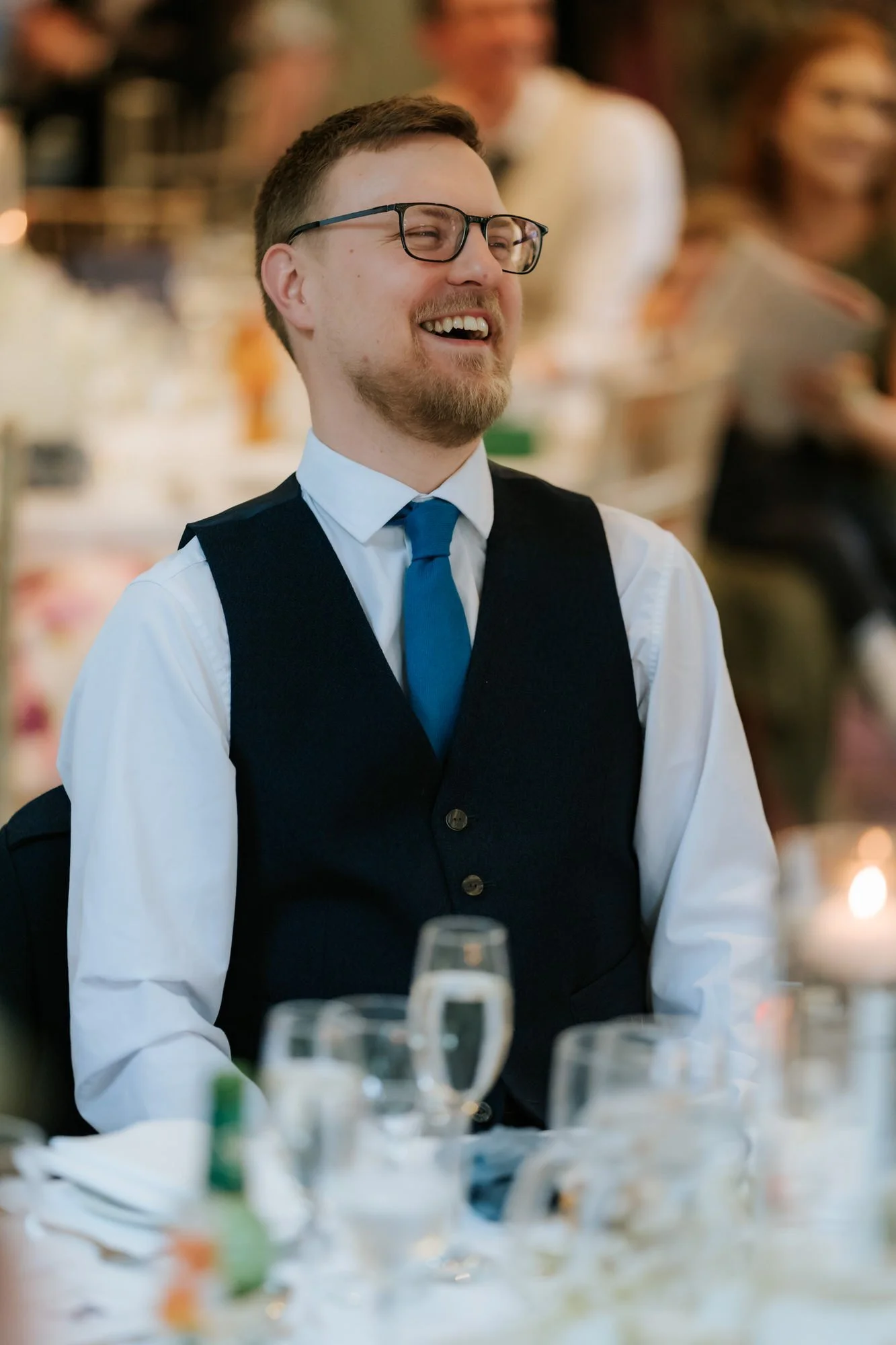 A guest with glasses reacting to the wedding speeches.