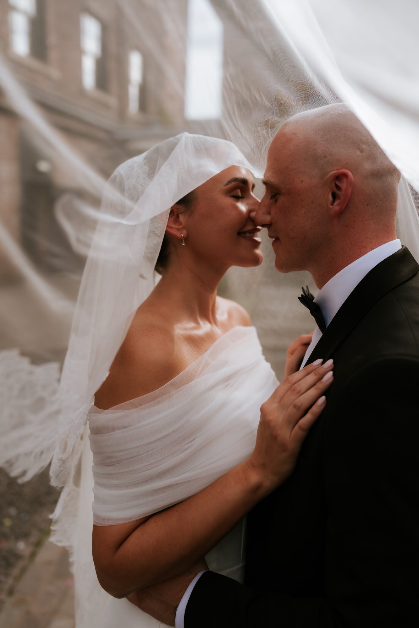 Caitlin and Craig laughing nose to nose beneath her veil.