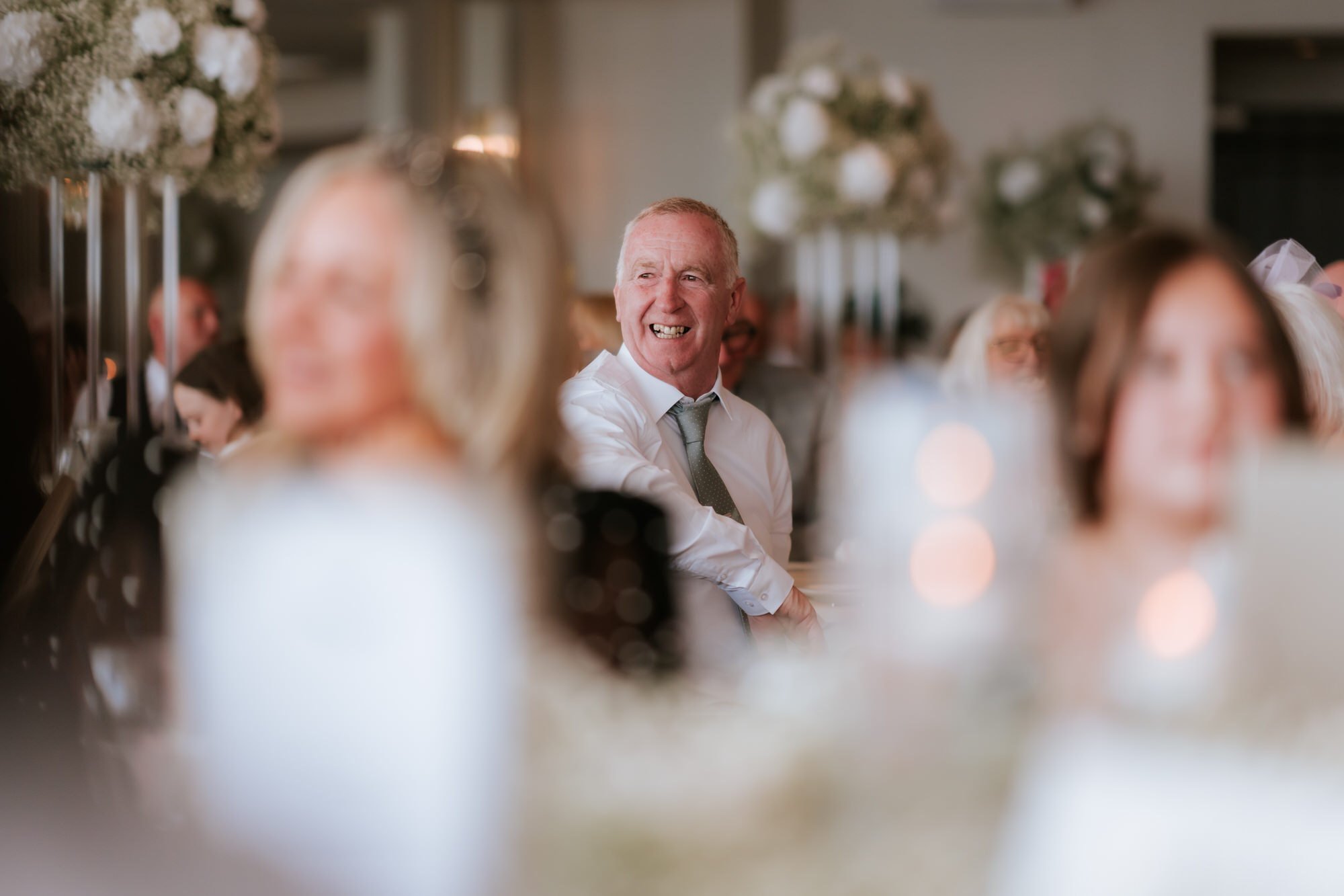 A guest laughing, framed through the reception flowers.