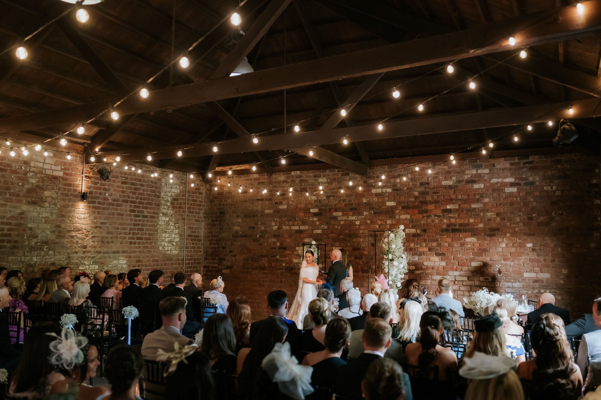 The Engine Works ceremony room with exposed brick, timber beams and festoon lights.