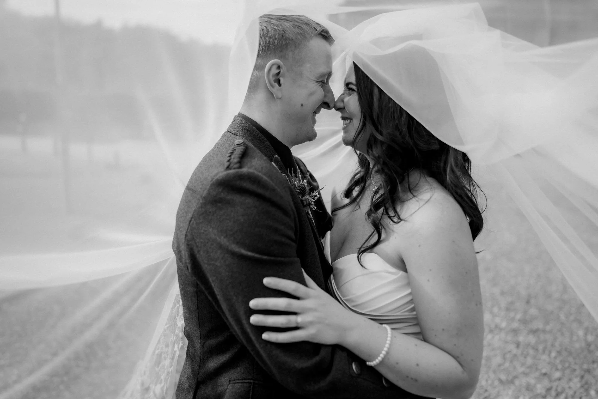 A close black and white portrait of Steph and Calum beneath the veil.