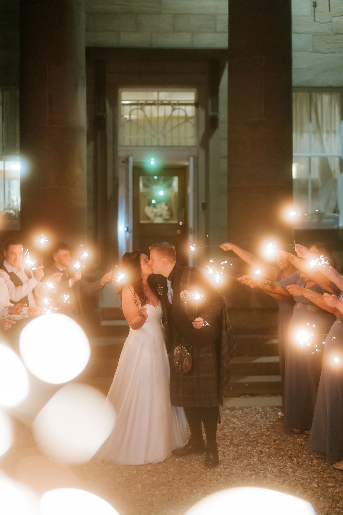 Steph and Calum kissing beneath a tunnel of sparklers.