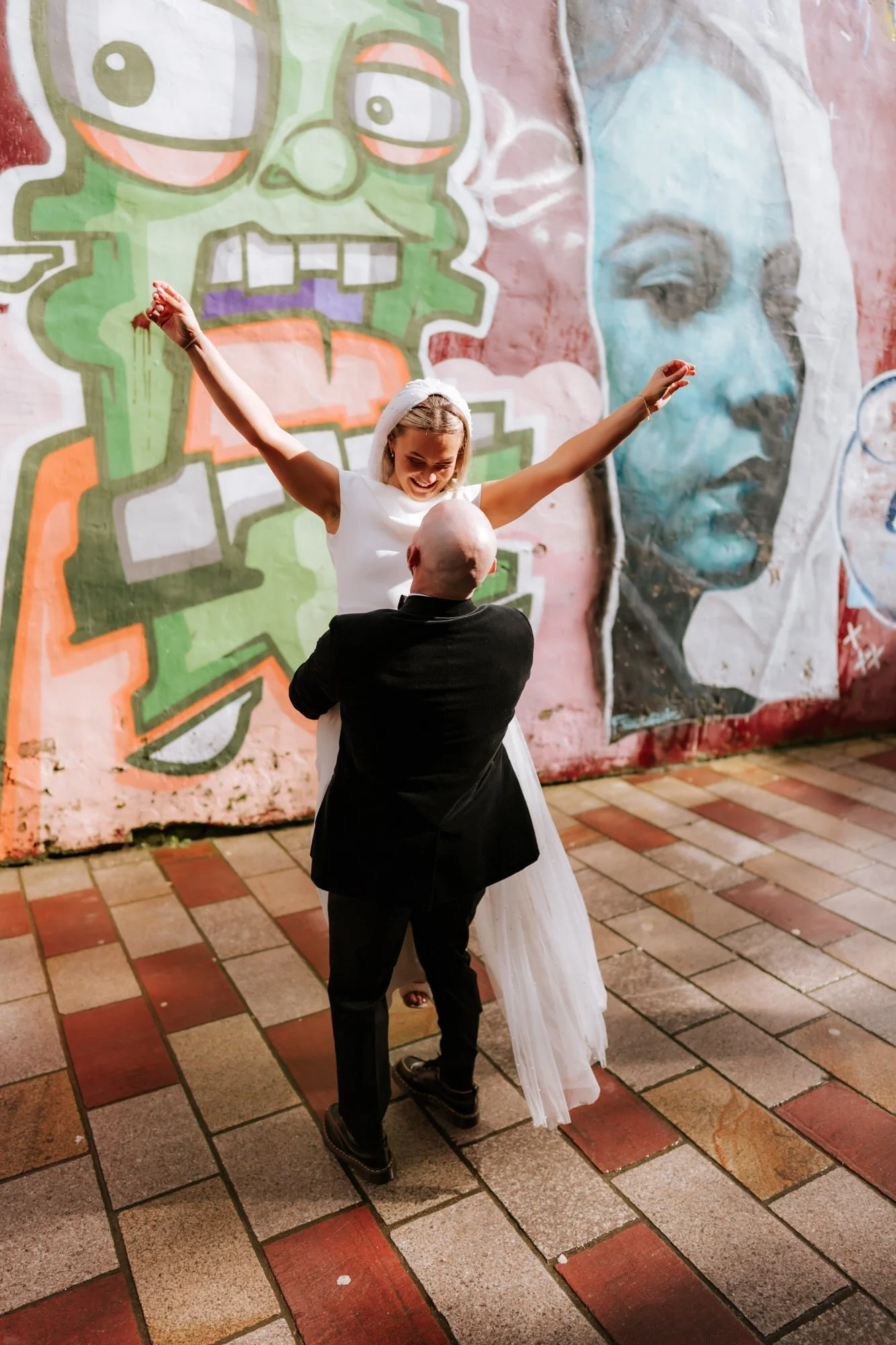 Ciaran lifting Rhona in front of colourful graffiti.