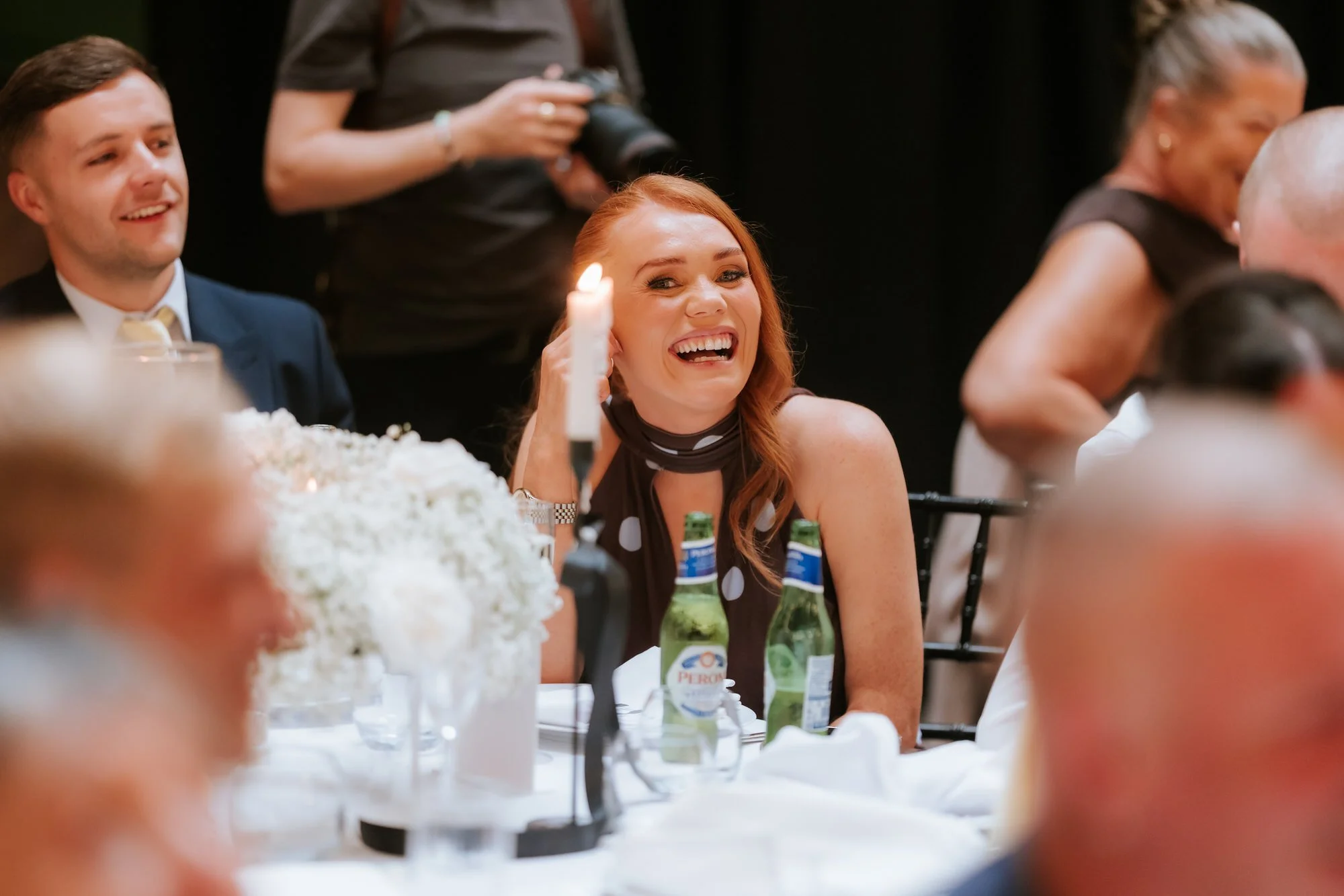 A guest laughing across a candlelit table at the wedding breakfast.
