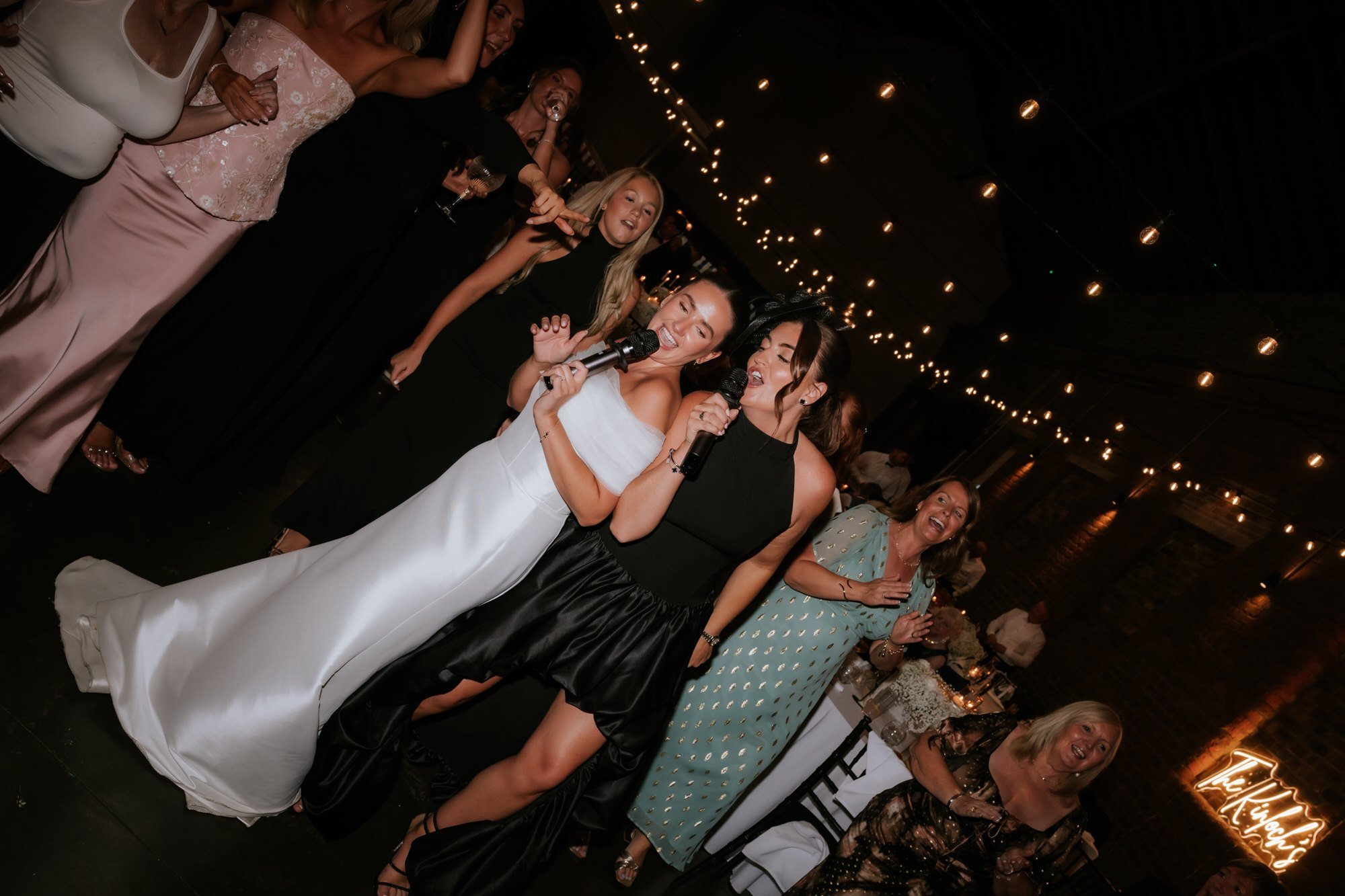 Caitlin and a friend singing into microphones surrounded by wedding guests.