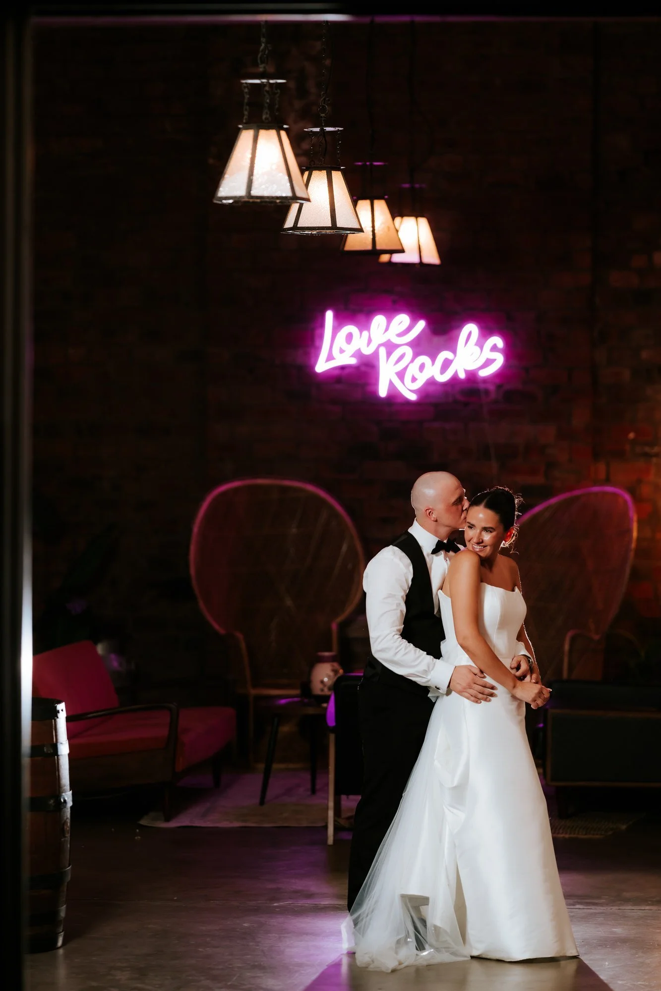 Craig kissing Caitlin beside the Love Rocks neon sign at The Engine Works.