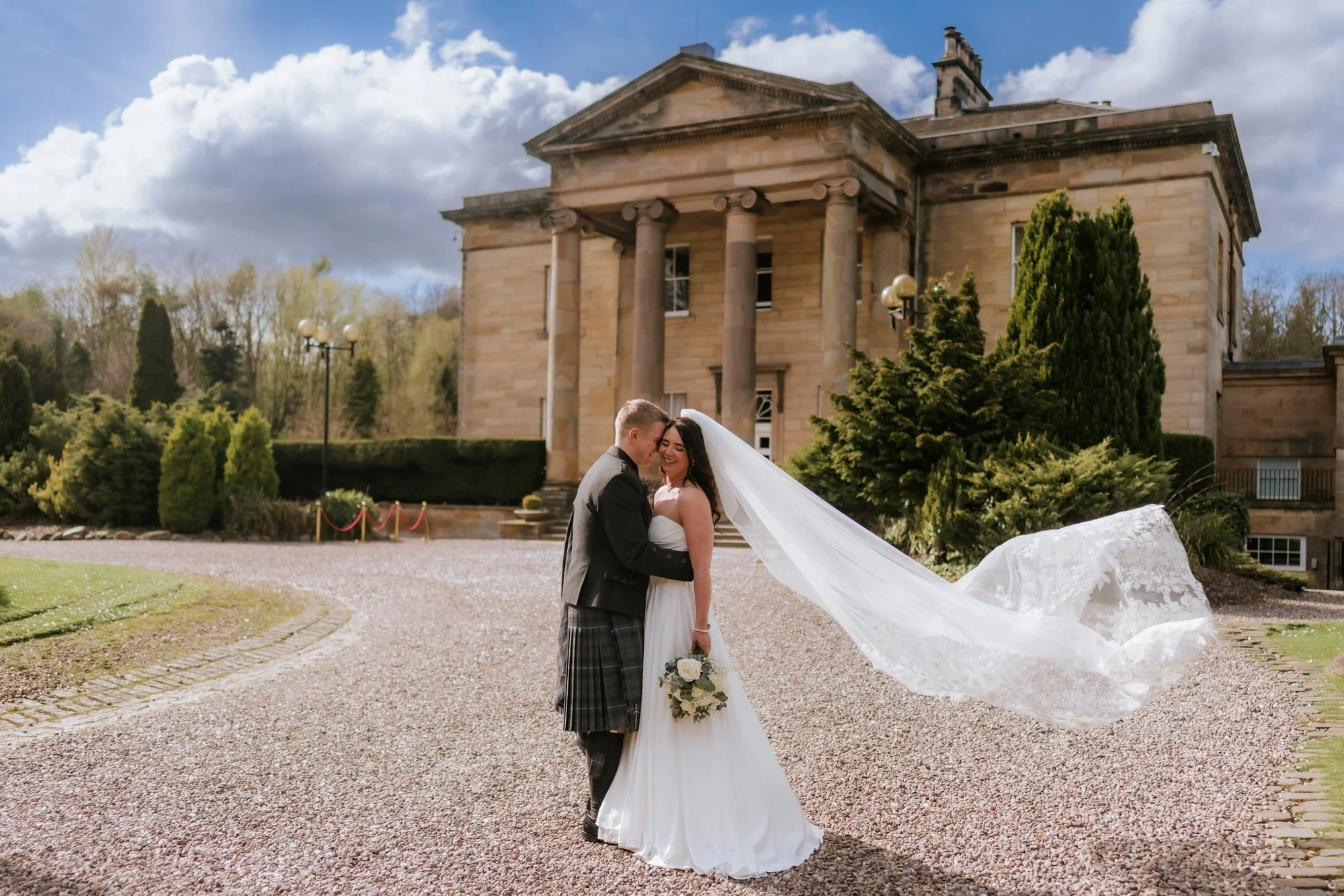 Steph and Calum beneath a flowing veil outside Balbirnie House.
