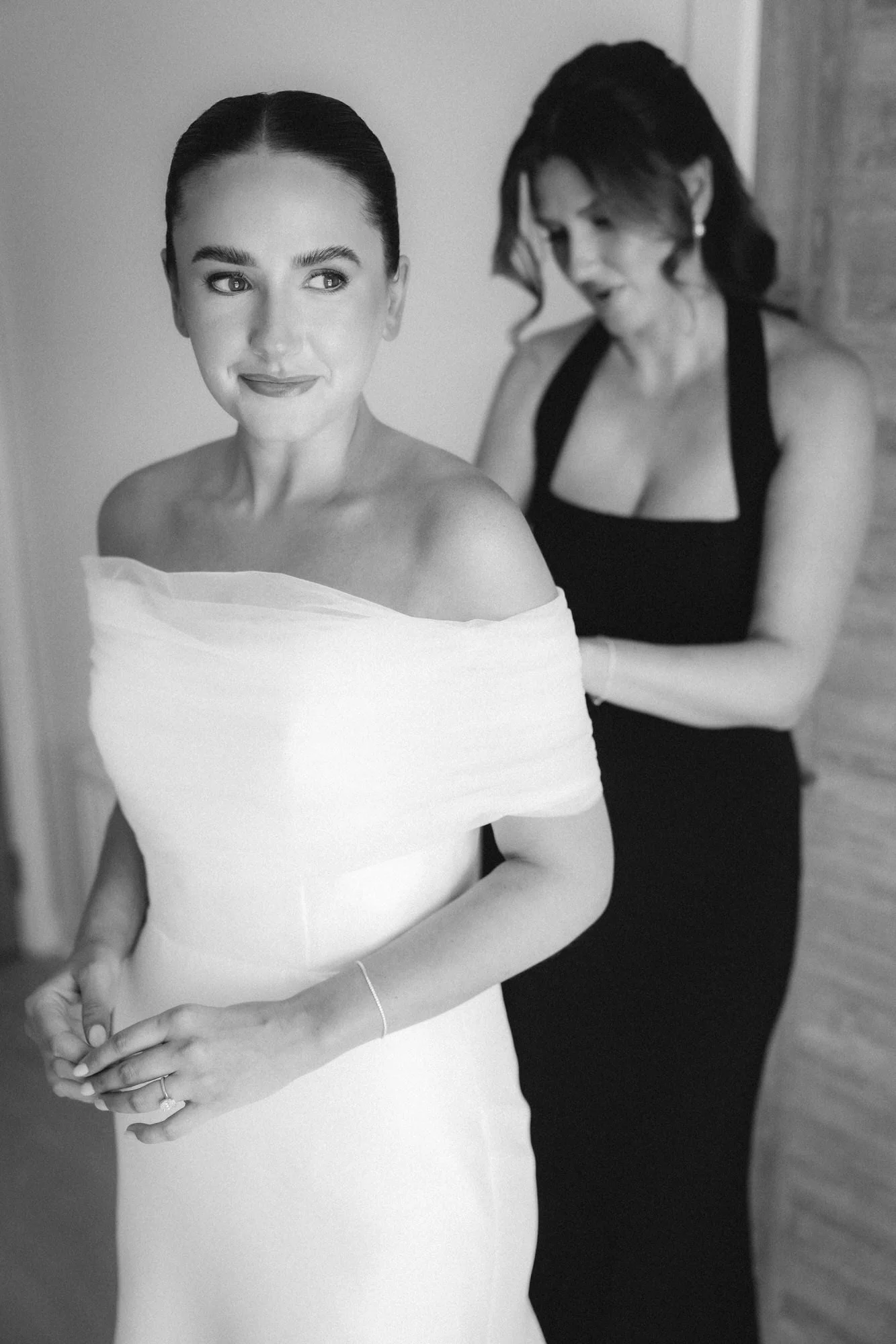 Black and white photograph of Caitlin having her wedding dress fastened.