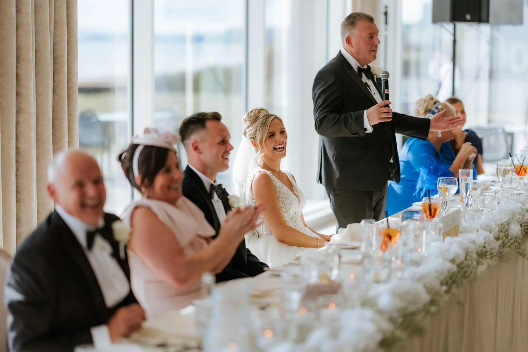 Nicole's dad giving his speech as the top table laughs.