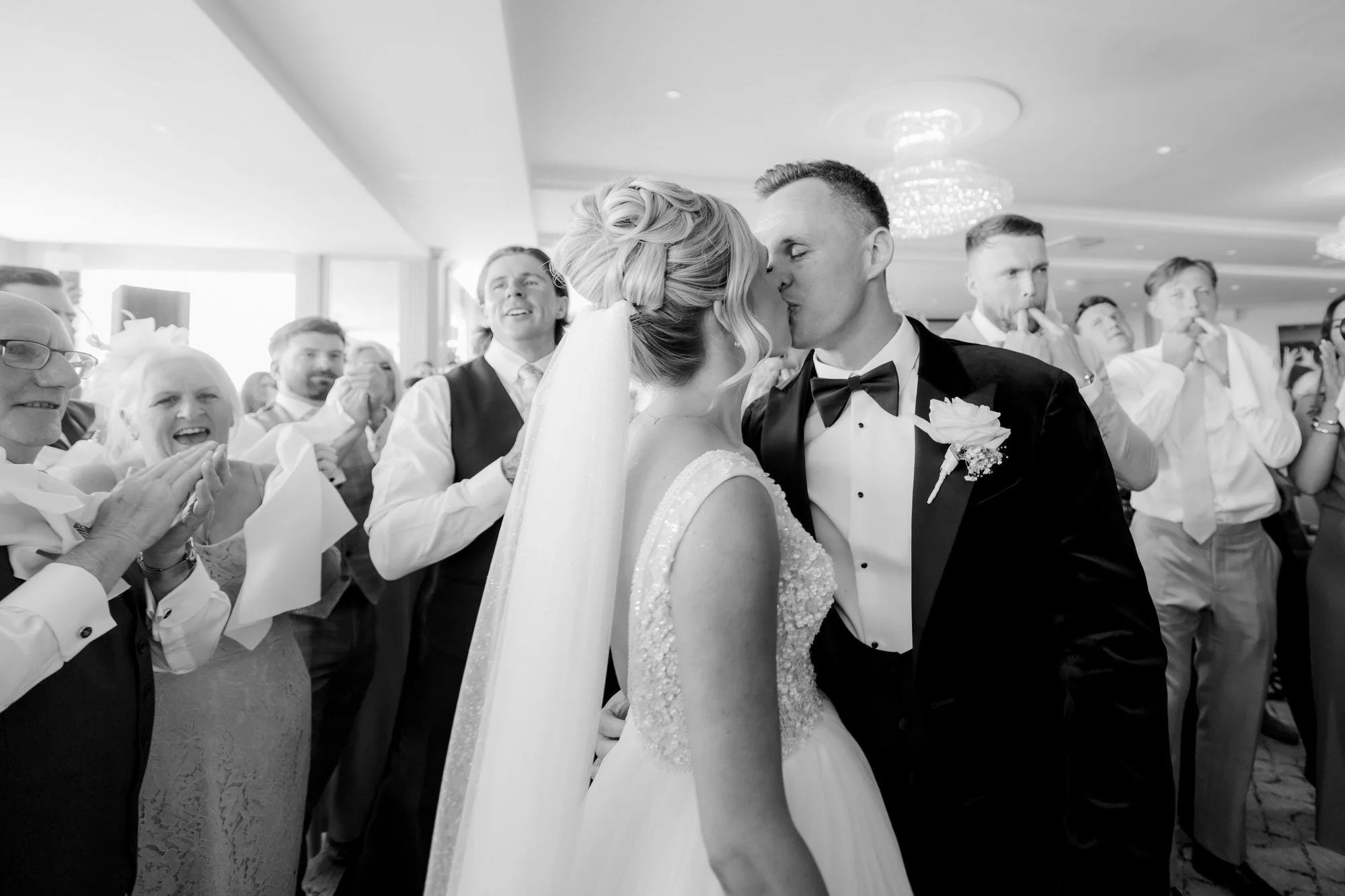 Nicole and Lawrence kissing amid cheering guests, photographed in black and white.