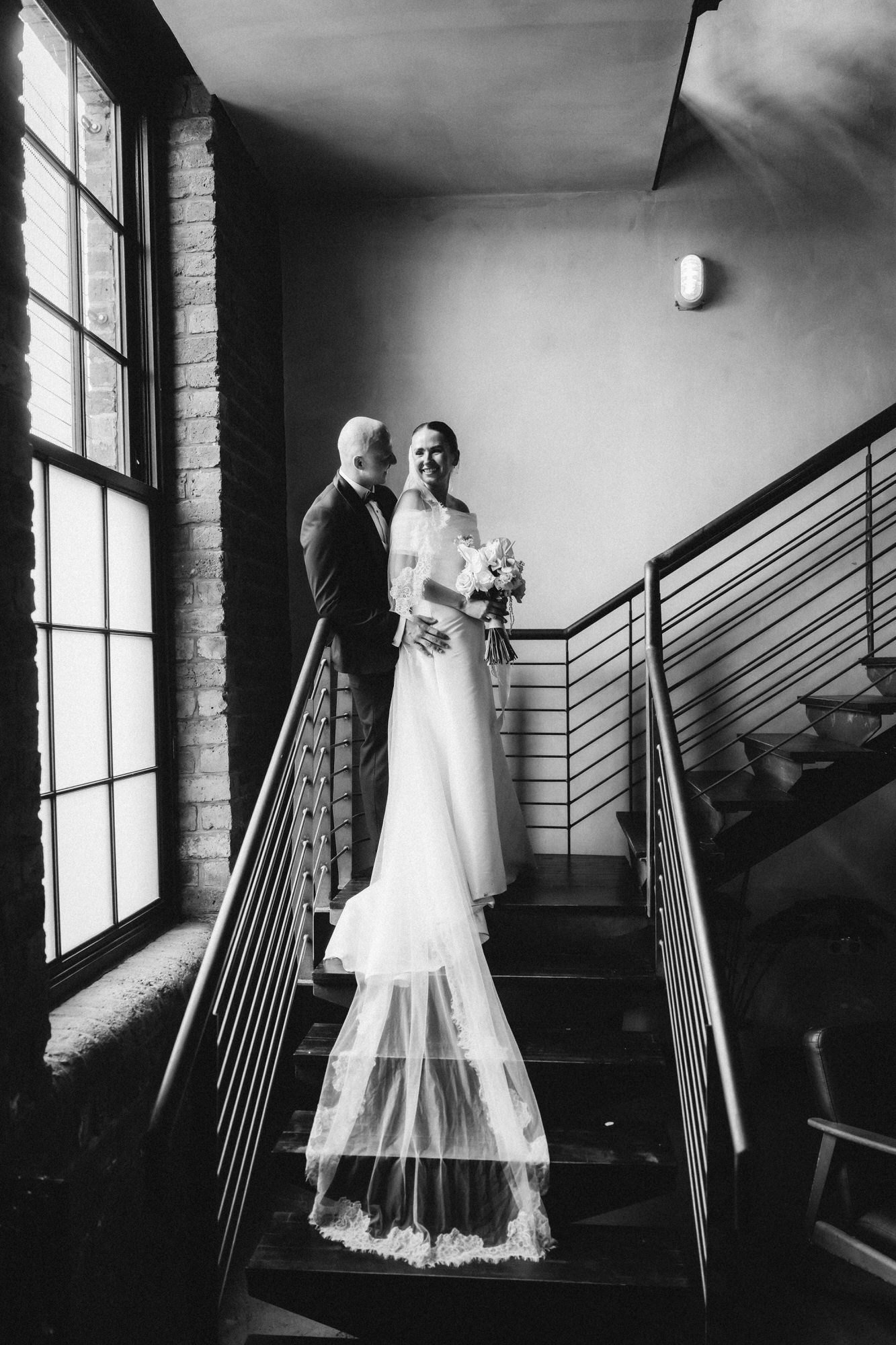 Caitlin and Craig smiling together on the staircase in black and white.