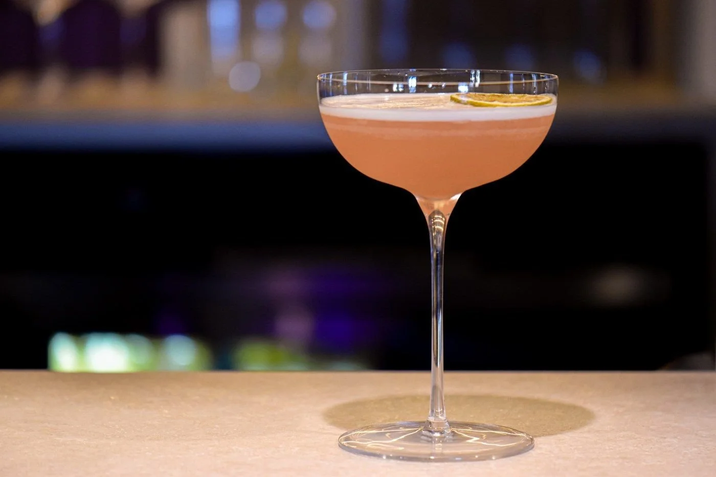 A pink cocktail in a coupe on the bar