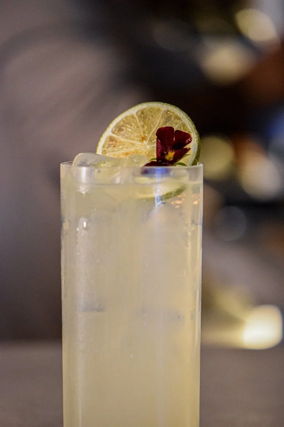 A tall highball with lime and a viola flower