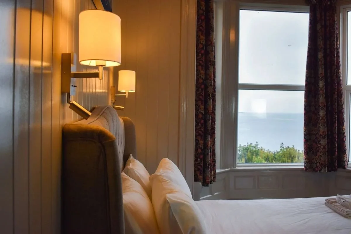 A sea-view room with warm wall lamps and the sea beyond the window