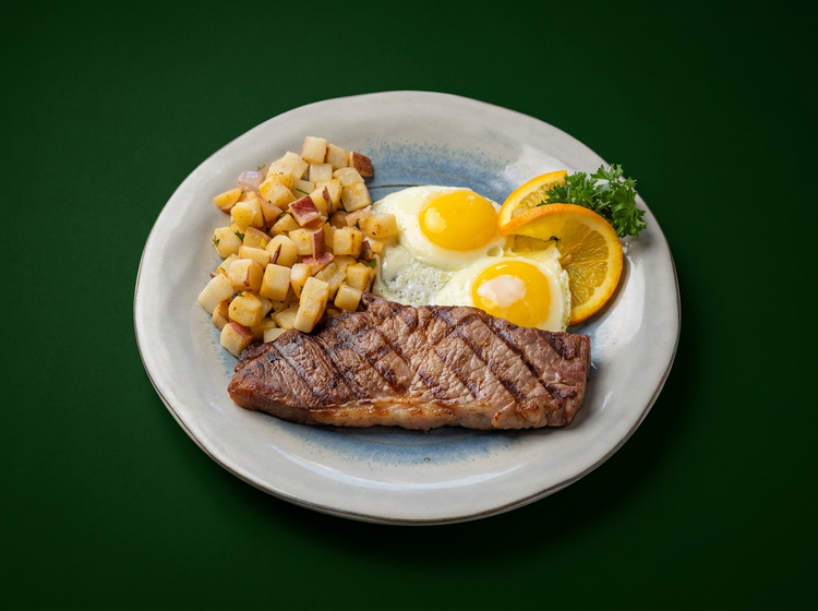 Grilled steak with two fried eggs and country potatoes