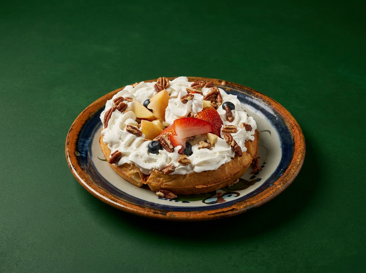 A waffle topped with whipped cream, fresh fruit and pecans