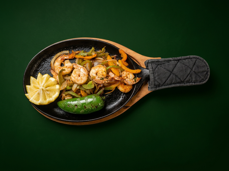 Shrimp fajitas with peppers, onions, lemon and a roasted pepper on a hot skillet