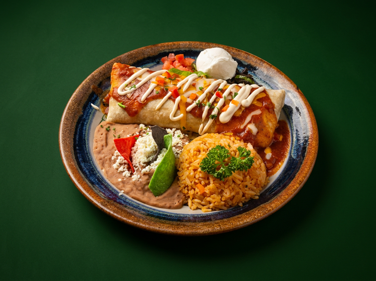 A burrito covered in ranchera sauce and crema, with Spanish rice and refried beans
