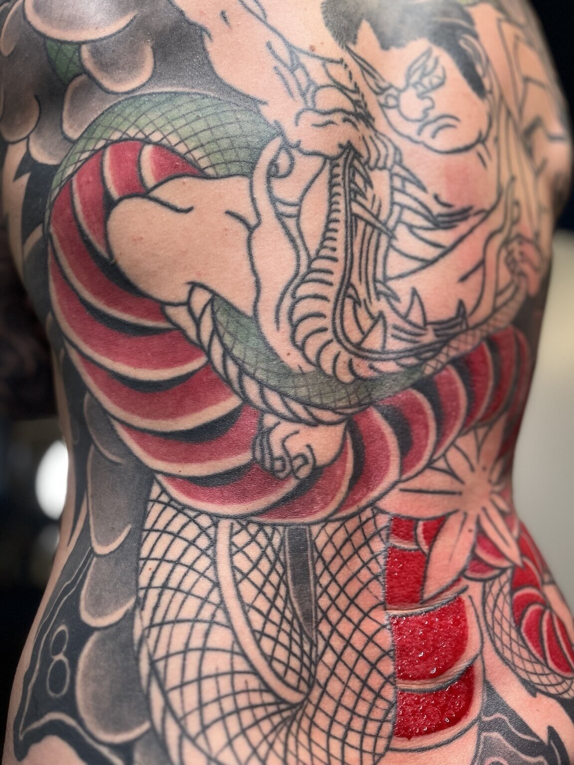 Detail of a colour Japanese snake tattoo with strong red and green areas.