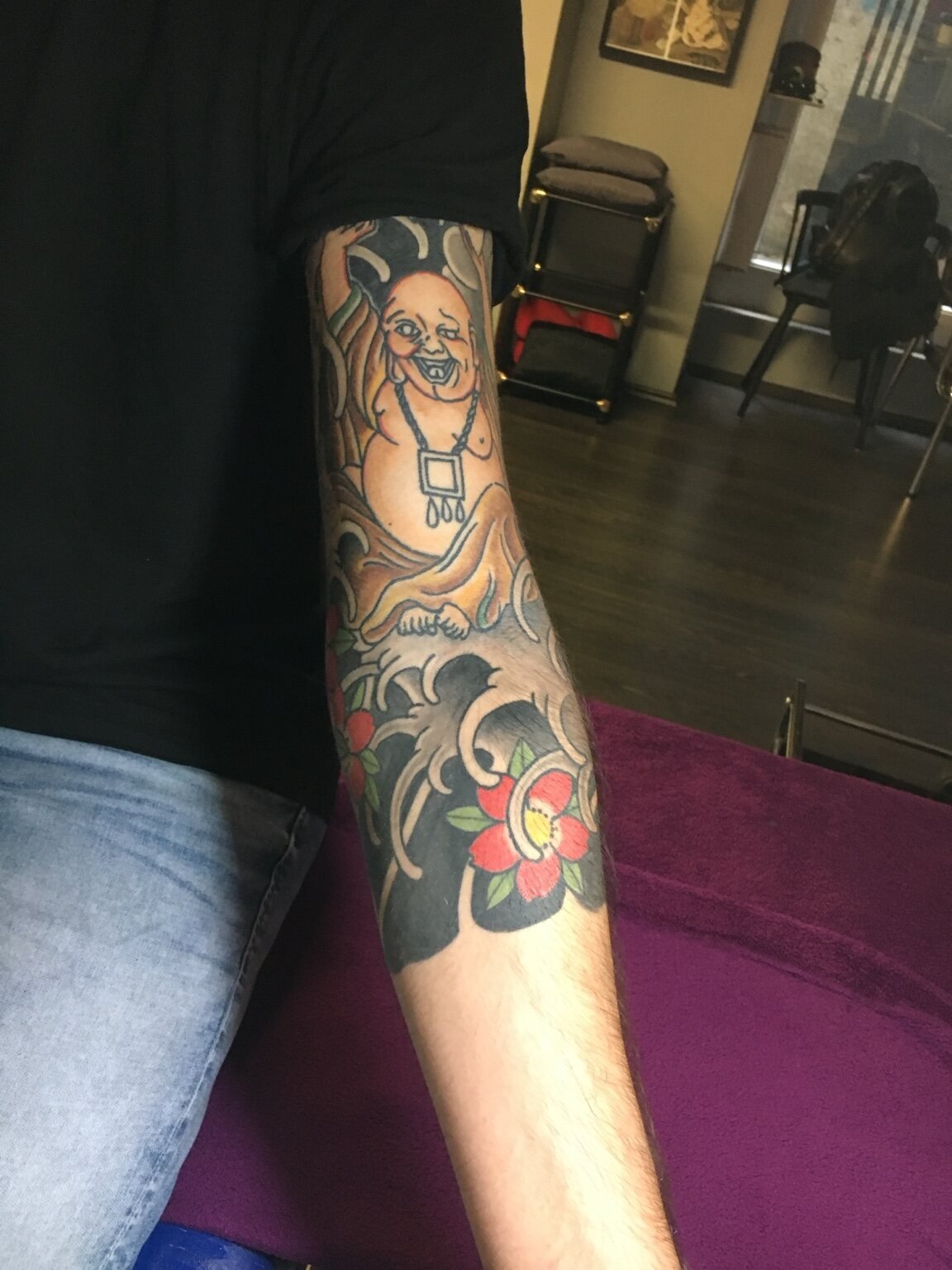 Colour Hotei tattoo with waves and flowers on the forearm.