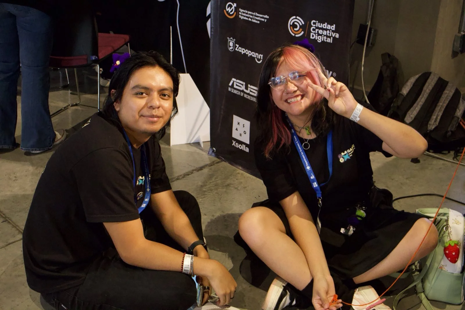 Dos asistentes de GCMX 2025 frente al backdrop de patrocinadores