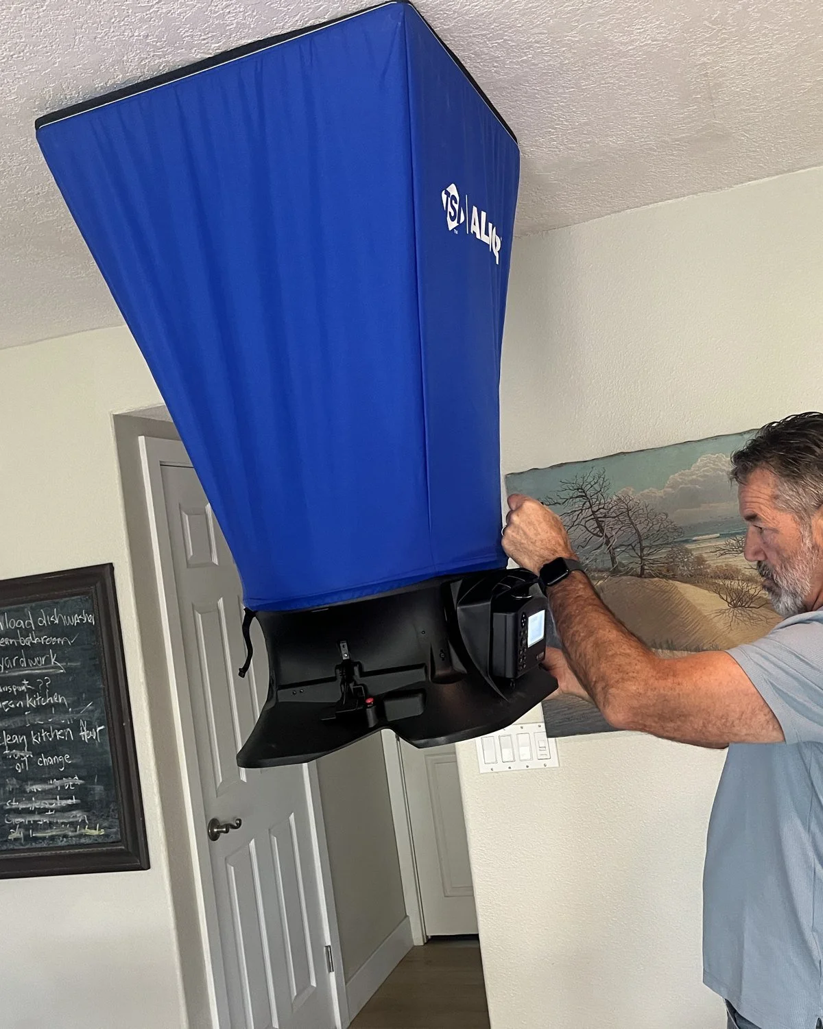 Rater holding a flow capture hood over a ceiling return to measure airflow