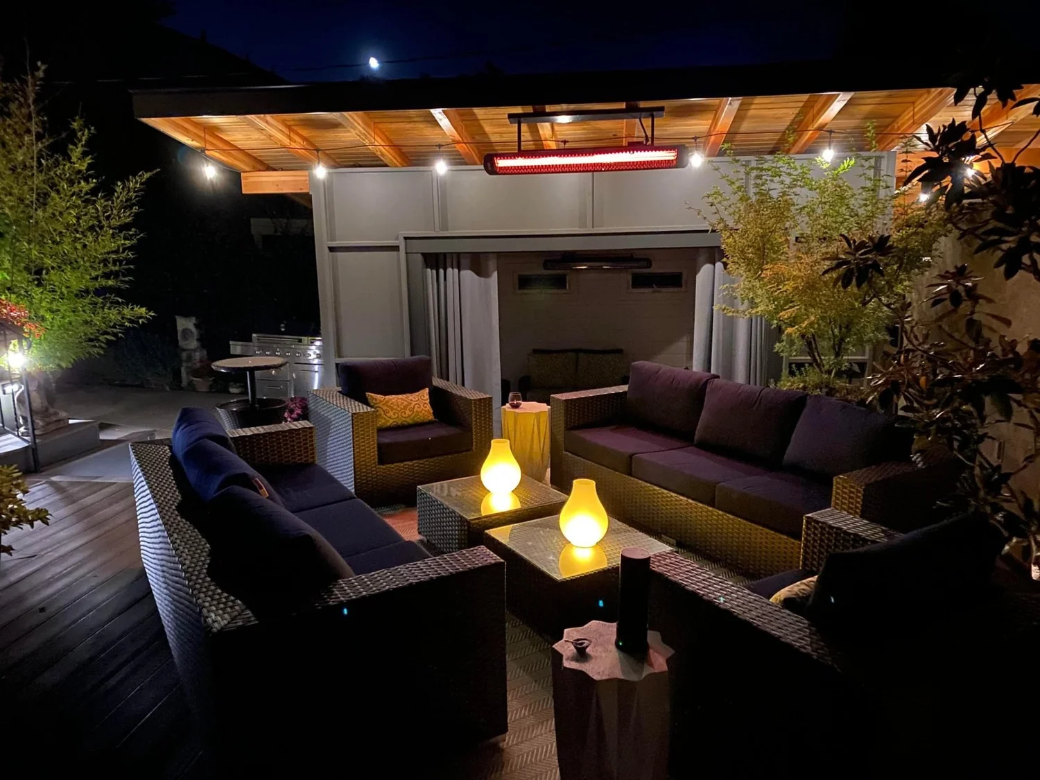 Covered backyard patio at night with heaters and string lights