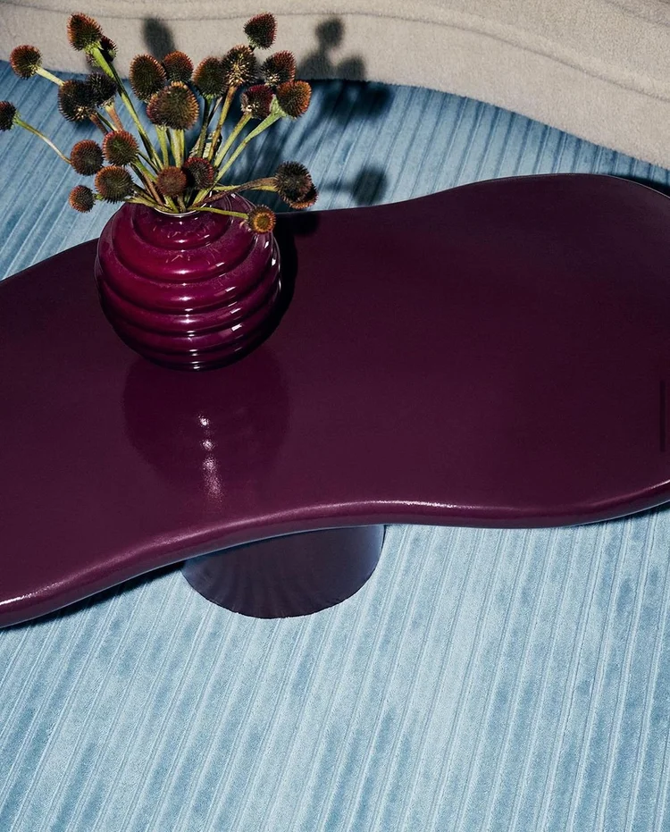Glossy plum table with dried seed heads on a blue rug