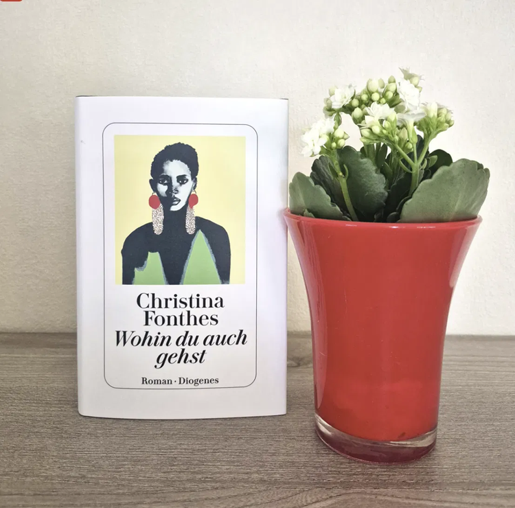 The Diogenes hardcover of Wohin du auch gehst with Ngozi on the cover, beside a red vase of white flowers
