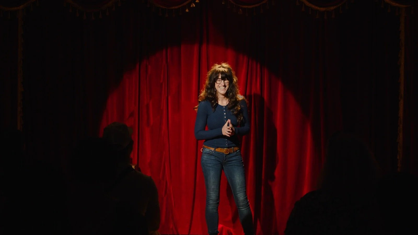 Jennifer on stage in a spotlight in front of a red curtain
