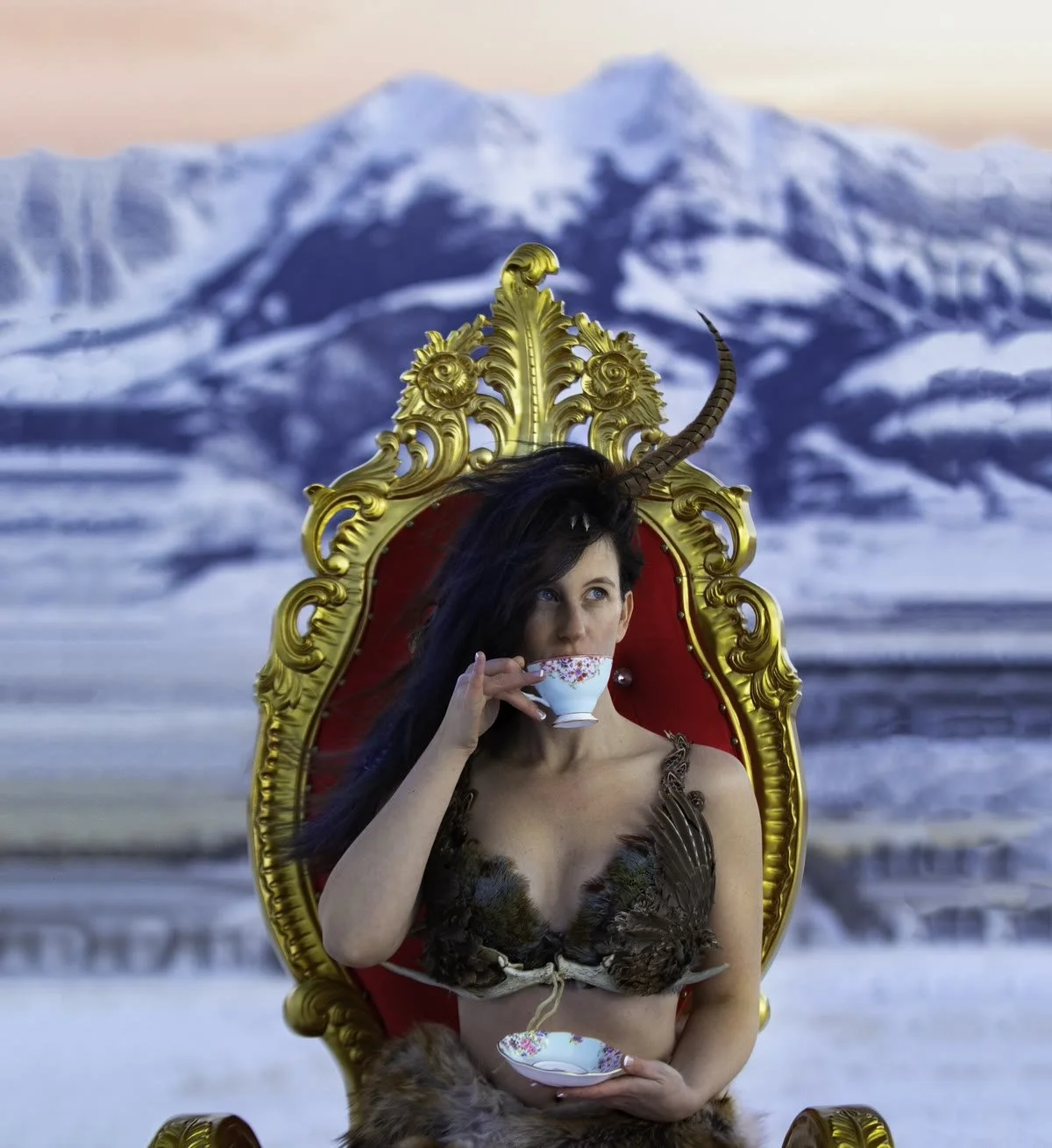 Jennifer on a gold throne sipping from a china teacup, snowy mountains behind