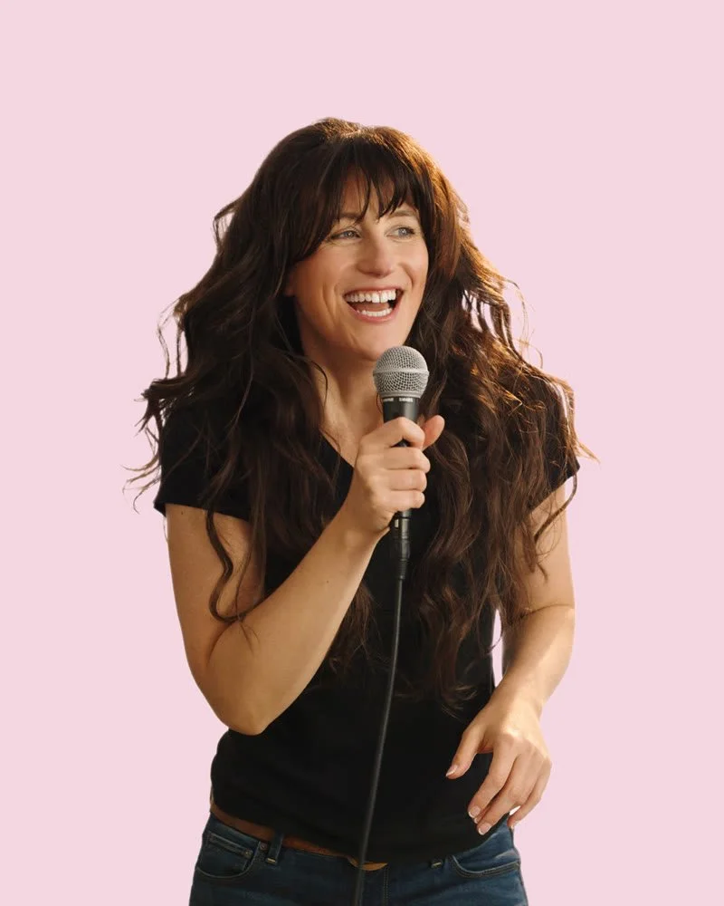 Jennifer laughing with a microphone on a pink background