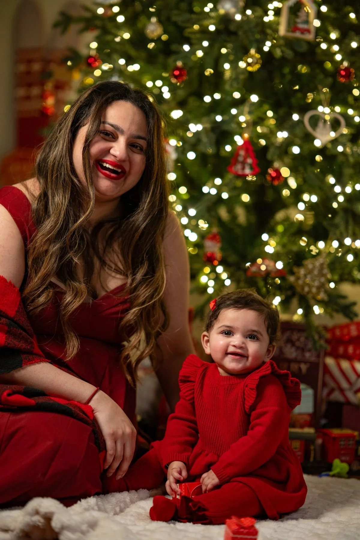 Mother and baby in red laughing in front of a lit Christmas tree at home