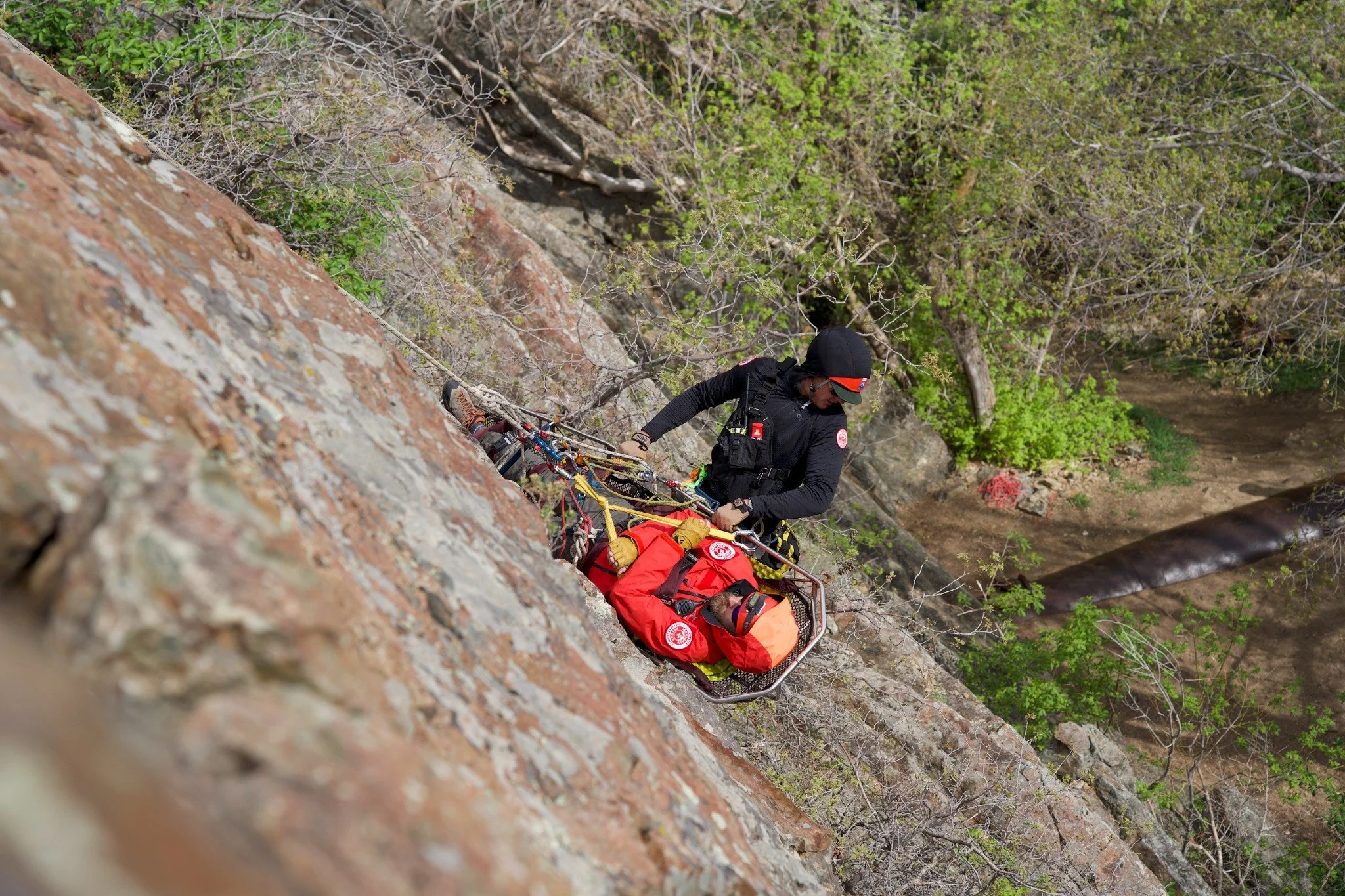 SLCOSAR members using a rope system and rescue litter on a rocky slope.