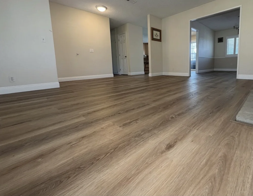Wide-plank flooring installed through an open living and dining area with white baseboards