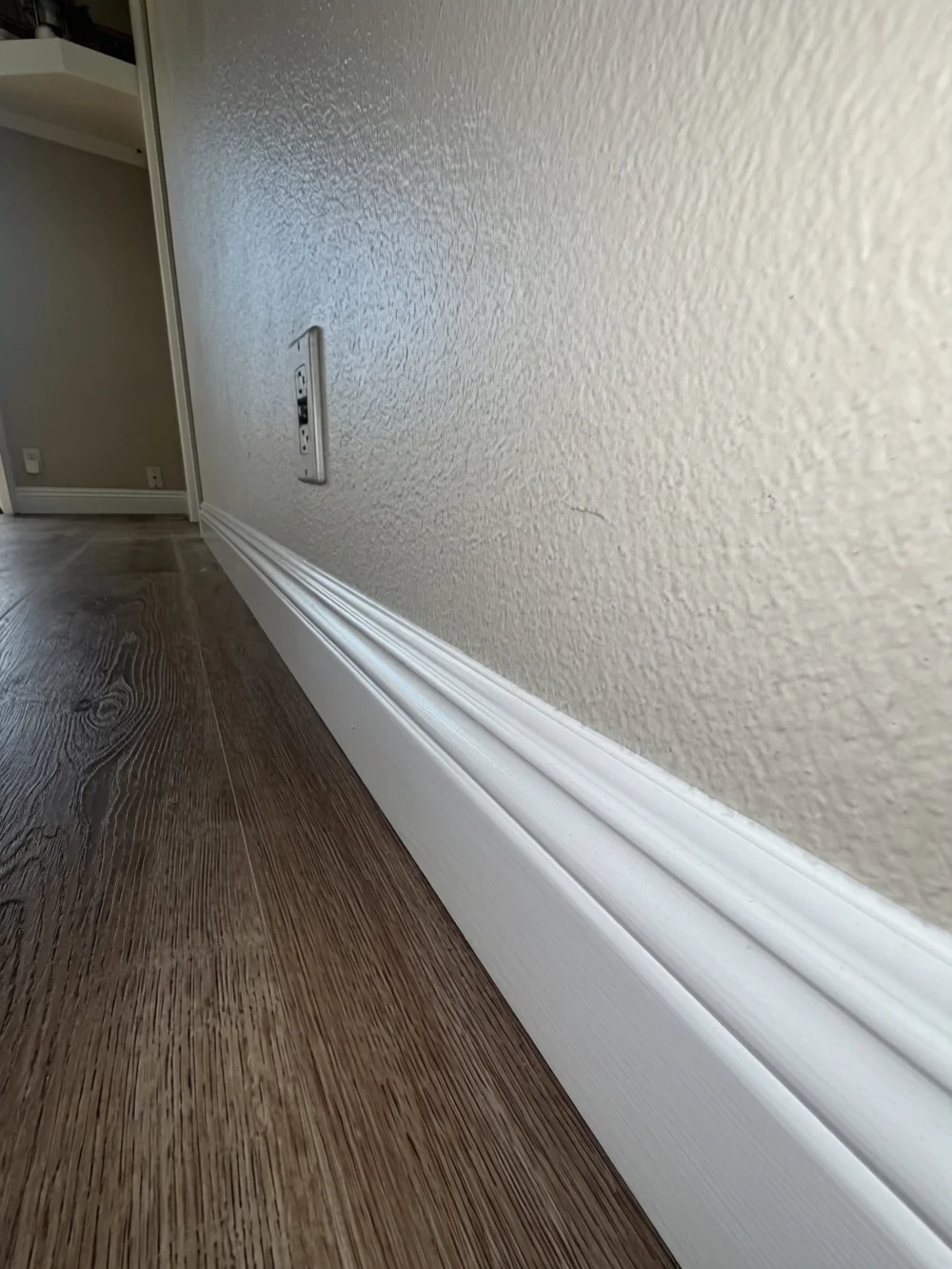 Close-up of wood-look plank flooring meeting a freshly painted white baseboard