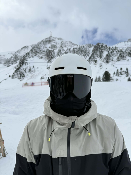 Skiløber med hvid hjelm og sort TORAN skibrille foran snedækket bjergtop