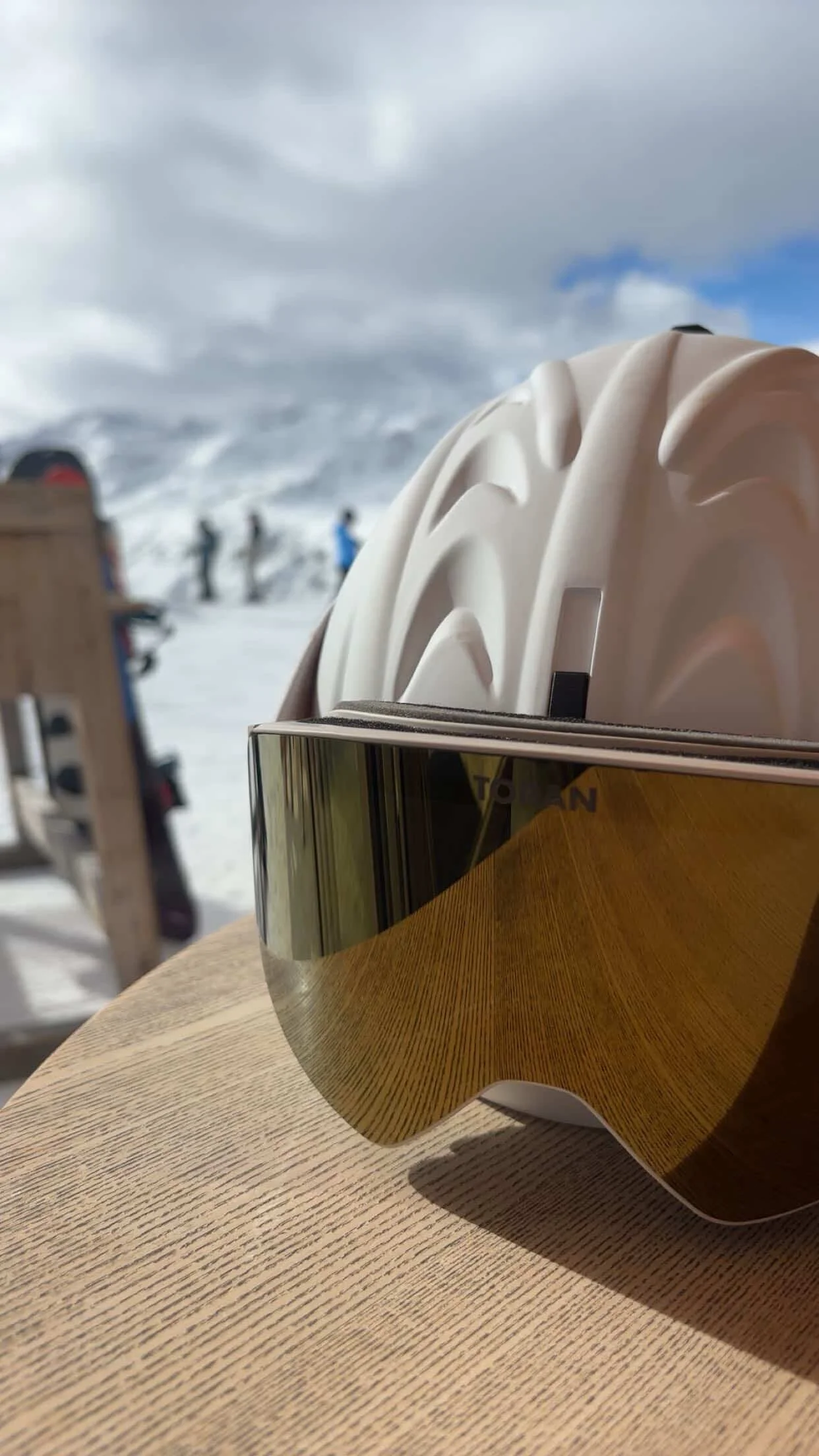 Detalje af beige skihjelm og TORAN skibrille med guld spejlglas mod bjergene
