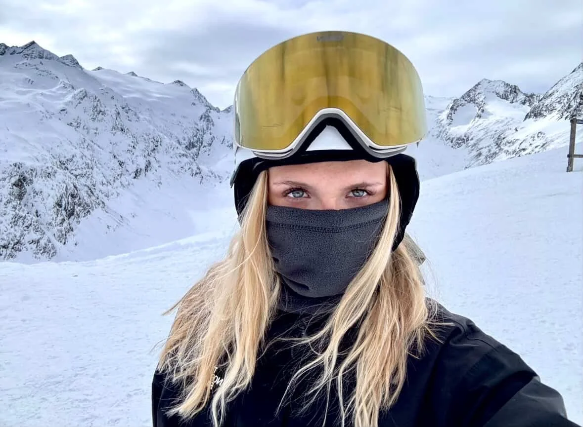 Kvinde med lyst hår og guld TORAN skibrille foran snedækkede bjerge
