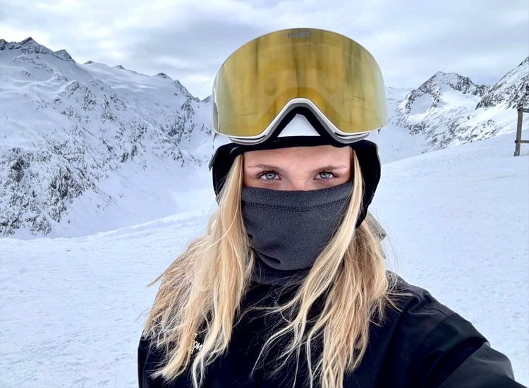 Kvinde med lyst hår og guld TORAN skibrille foran snedækkede bjerge