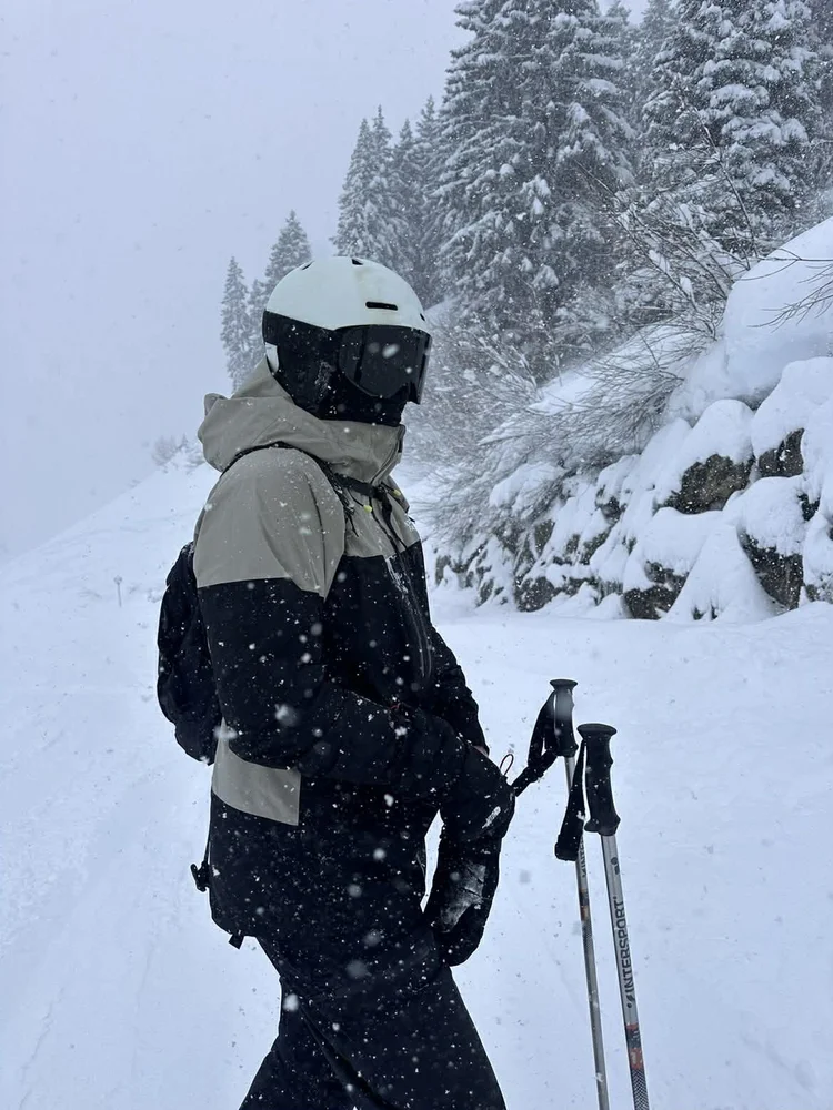 Skiløber med hvid hjelm og TORAN skibrille i snefald mellem snedækkede graner
