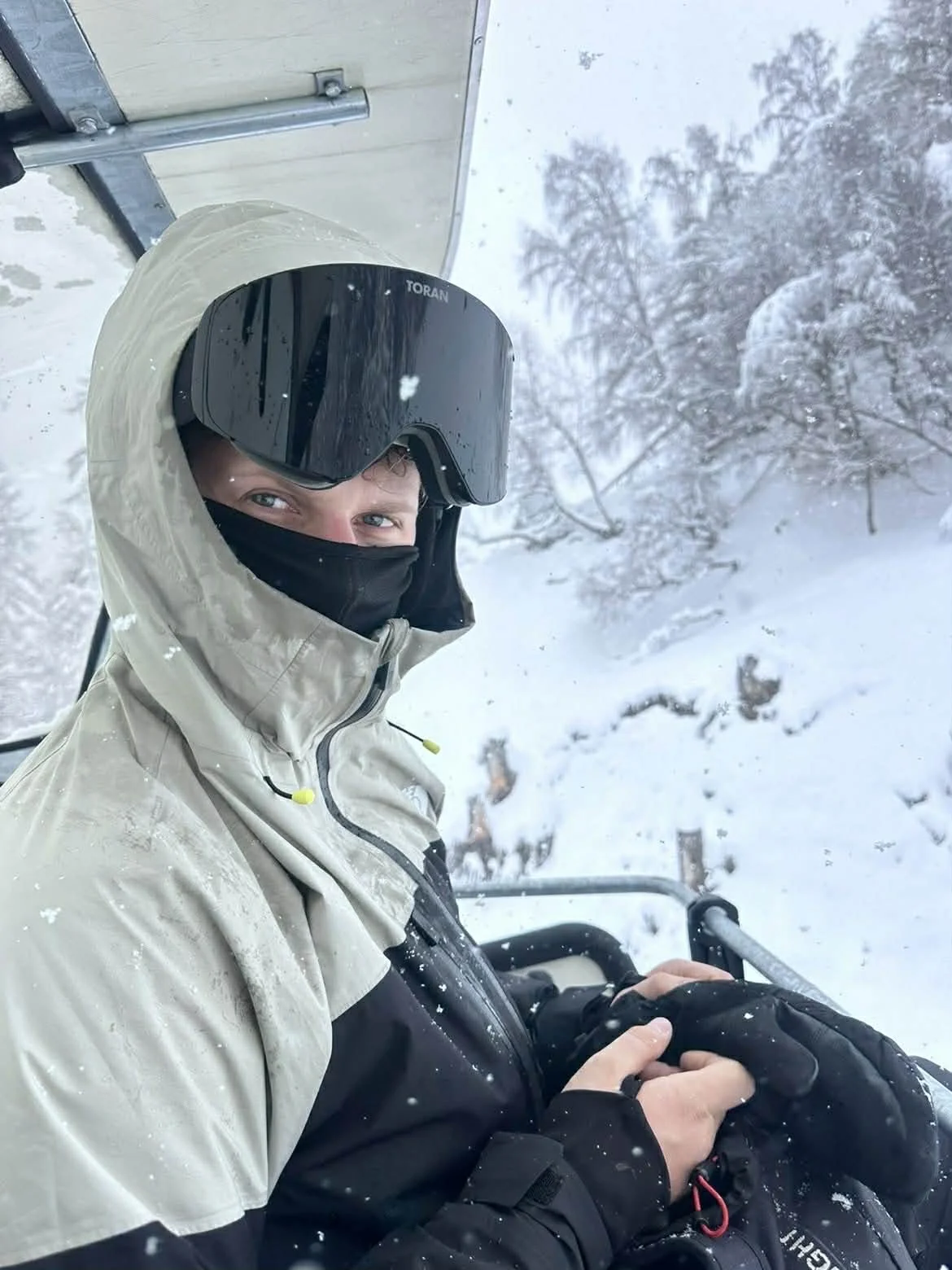 Skiløber med hætte og sort TORAN skibrille i stoleliften under snefald