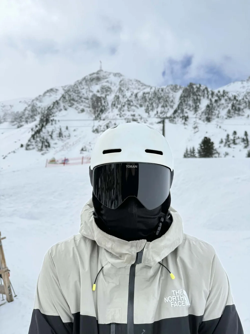 Skiløber med sort TORAN skibrille og halsedisse foran snedækkede tinder