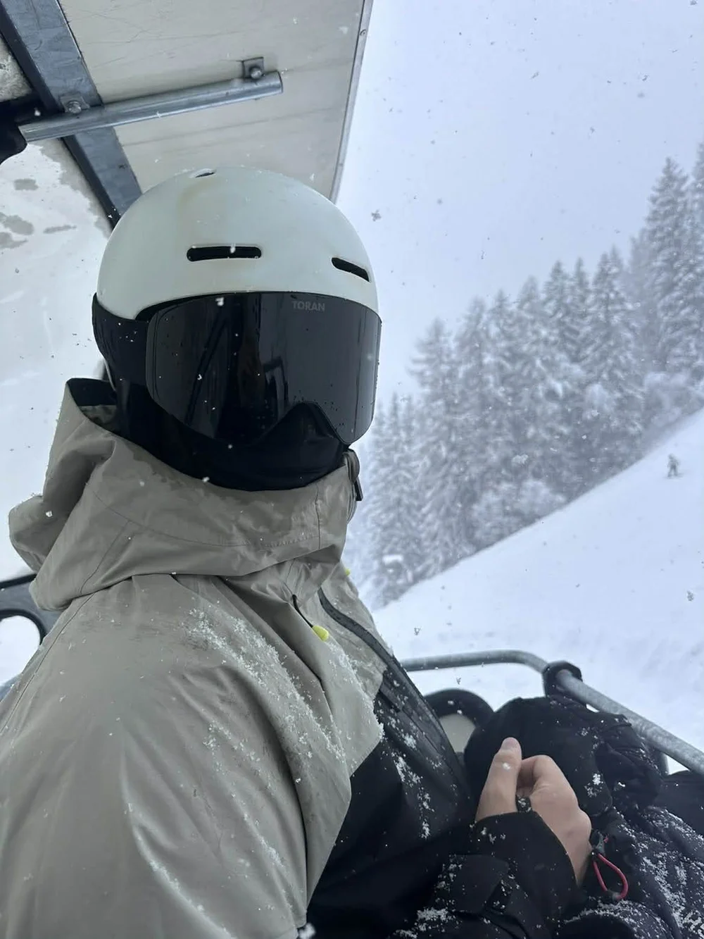 Skiløber i stoleliften med TORAN skibrille og hvid hjelm under snefald