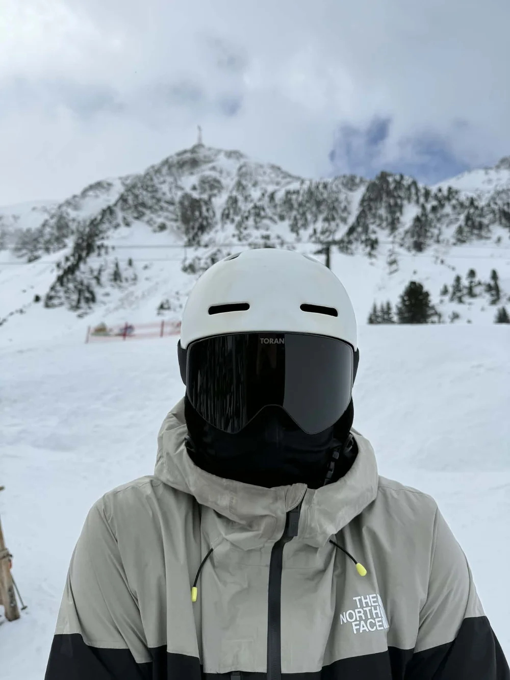 Portræt af skiløber med sort TORAN skibrille foran bjerglandskab i overskyet vejr