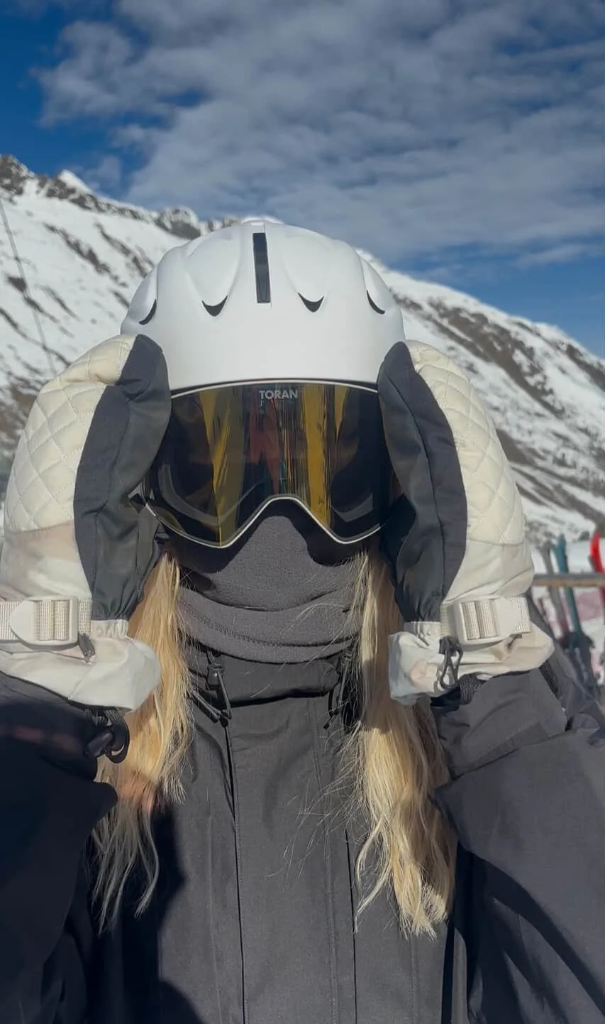 Kvinde med hvid hjelm og TORAN skibrille i solskin på toppen af bjerget