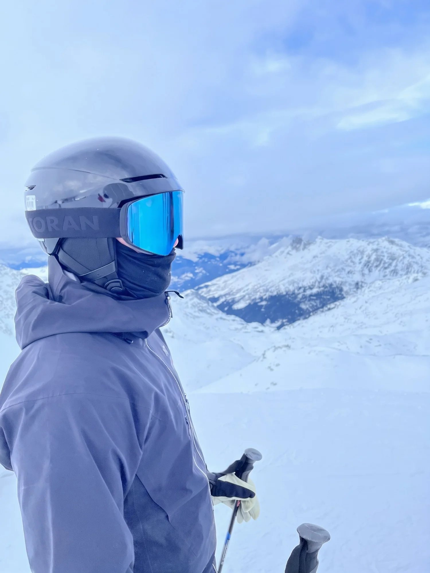 Skiløber i lilla jakke med TORAN skibrille med blåt spejlglas på pisten med bjergudsigt